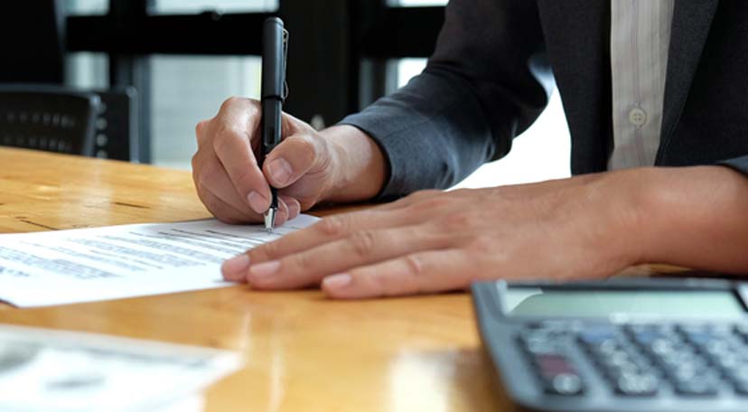 An individual signing a contract, with a calculator on the table